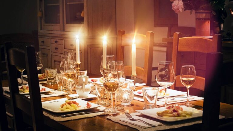 Dining table set for a meal with lit candles, wine glasses, and plated dishes in a warmly lit room