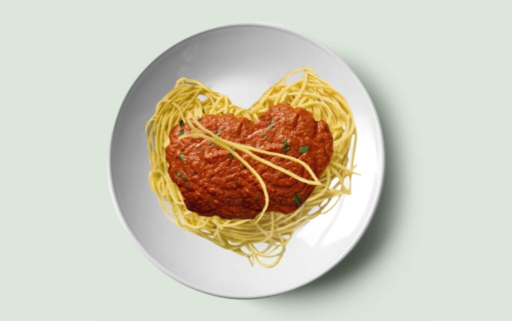 A plate with spaghetti and tomato sauce in the shape of a heart.