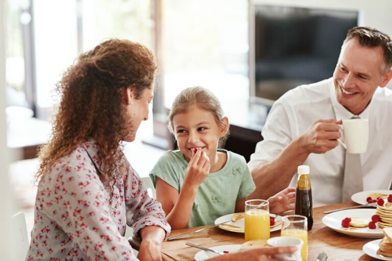A family of three have a conversation as they eat breakfast at the table.