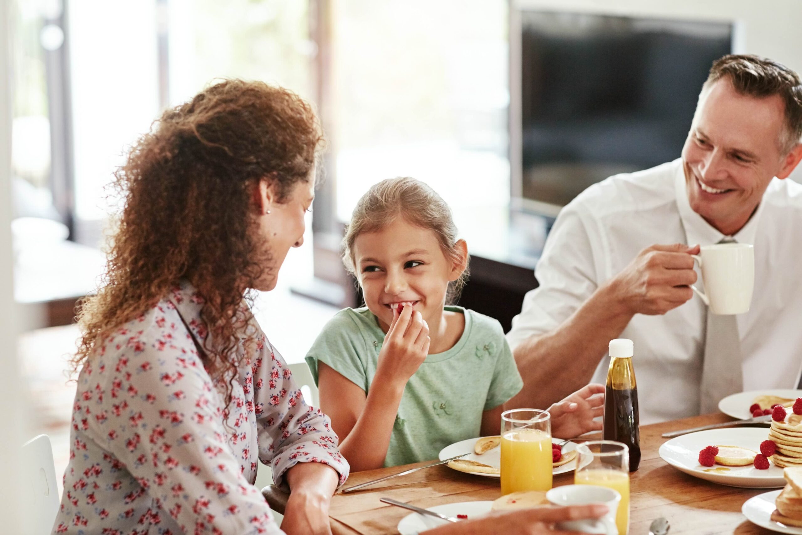 A family of three have a conversation as they eat breakfast at the table.