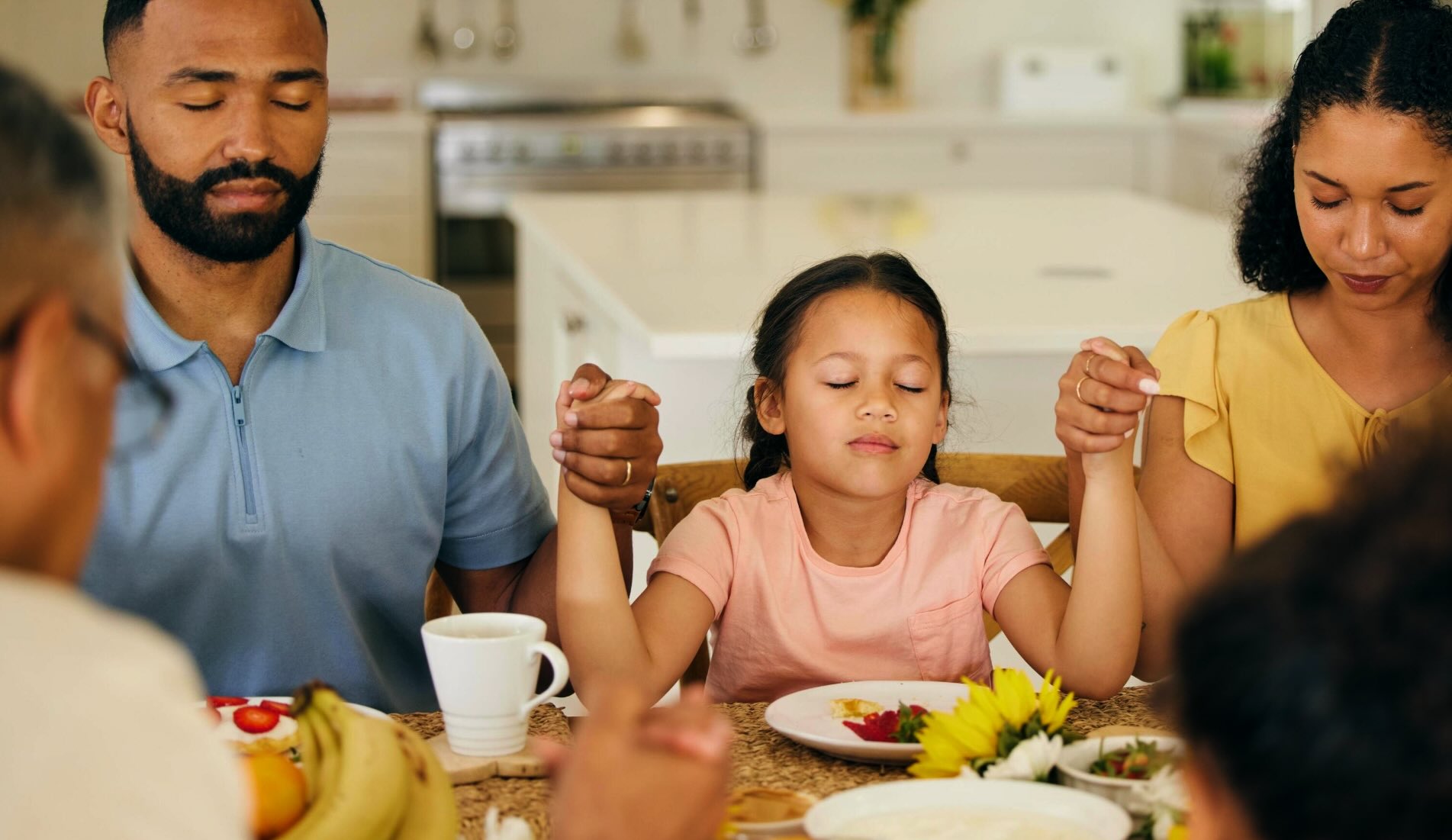A family holds hands at a dinner table saying a prayer.