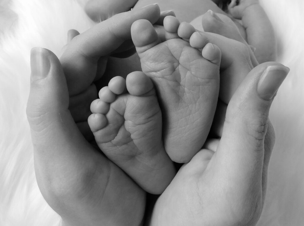 Black-and-white close-up of an adult’s hands gently holding a newborn baby’s feet.